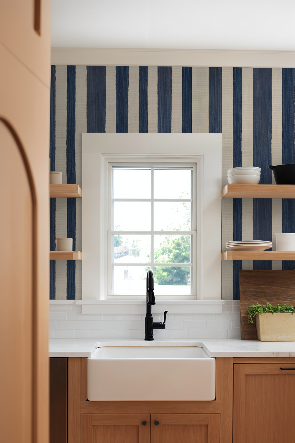 Modern kitchen with blue and beige striped wallpaper, white sink, wooden shelves.