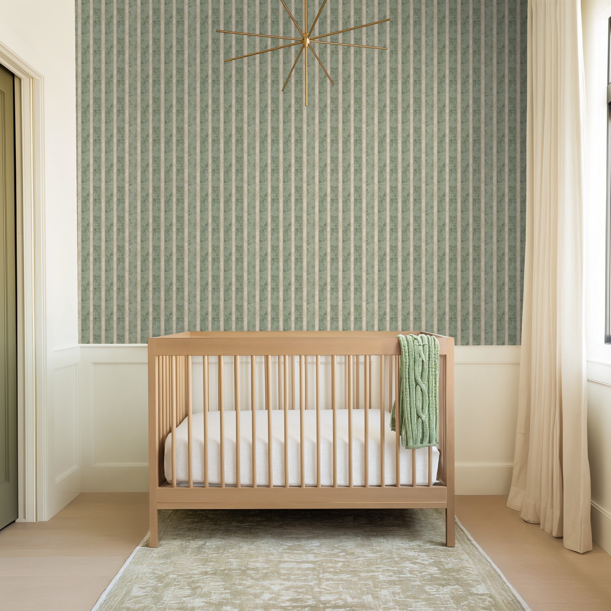 Nursery with muted sage and cream striped wallpaper, wooden crib, and green blanket.