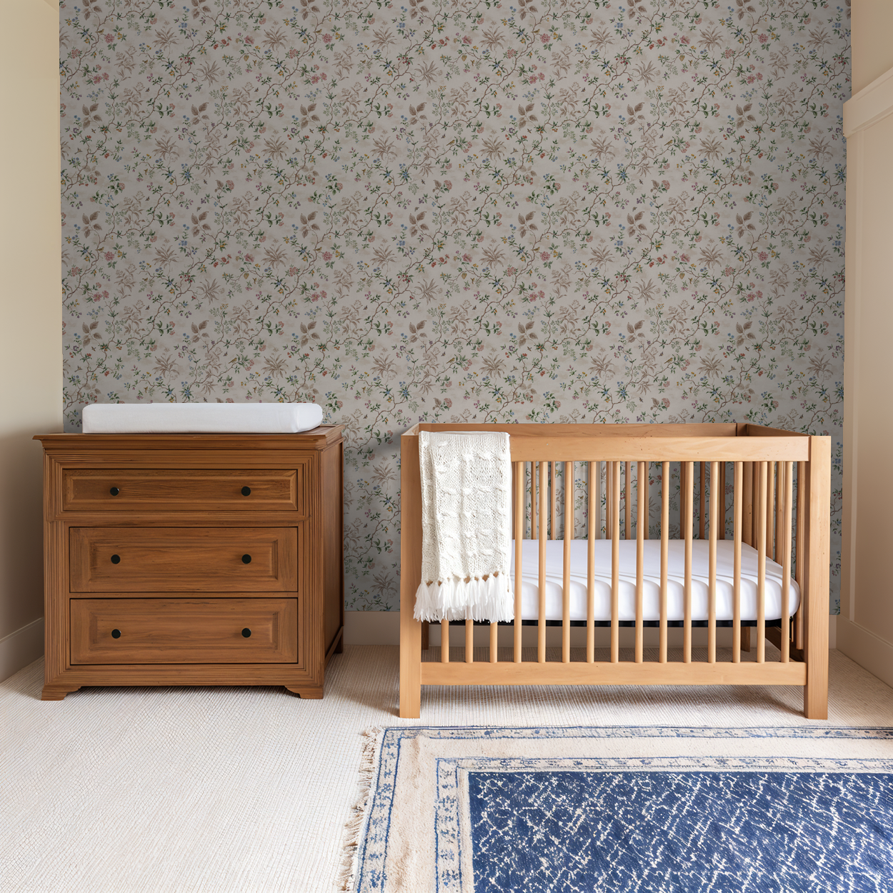 Floral wallpaper with vines and blossoms in nursery with wooden crib and dresser.
