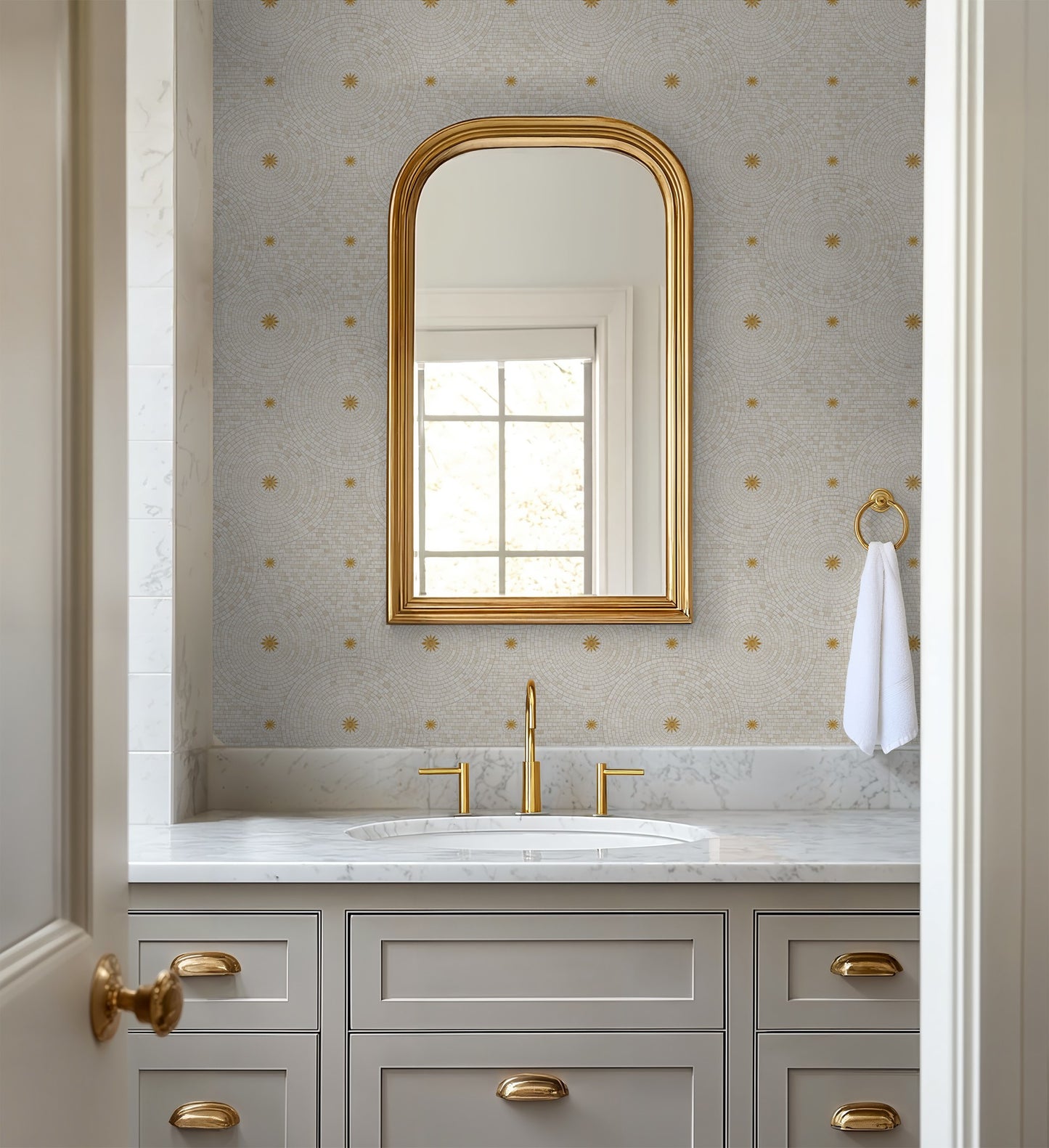 Bathroom with gold-accented mirror and geometric cream and gold wallpaper.